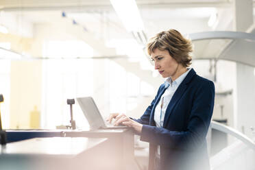 Mature female entrepreneur using laptop while working at industry - JOSEF04321