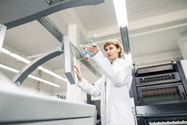Female Scientist with molecule model operating machine in industry - JOSEF04331