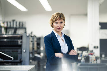 Confident businesswoman standing with arms crossed in printing factory - JOSEF04348
