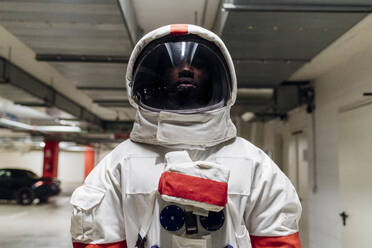 Mid adult astronaut wearing space helmet standing in parking lot - MEUF02687