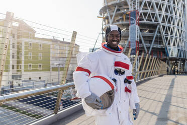 Lächelnder männlicher Astronaut mit Weltraumhelm auf einer Brücke in der Stadt stehend - MEUF02714