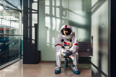 Male astronaut waiting on bench in corridor - MEUF02727