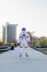 Männlicher Astronaut springt in einem öffentlichen Park - MEUF02734