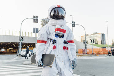 Männlicher Astronaut mit Skateboard am Zebrastreifen in der Stadt - MEUF02740