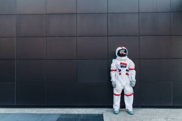 Male astronaut standing in front of black wall at footpath - MEUF02741