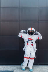 Männlicher Astronaut, der seinen Bizeps vor einer schwarzen Wand beugt - MEUF02742