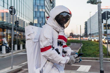 Männlicher Astronaut im Raumanzug, der auf einer Straße in der Stadt ein Mobiltelefon benutzt - MEUF02752