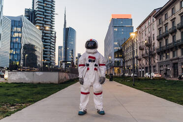 Männlicher Astronaut steht auf einem Fußweg inmitten von Gebäuden - MEUF02754