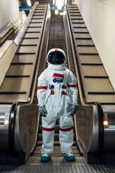 Mid adult astronaut standing in front of escalator - MEUF02764