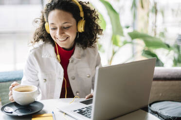 Smiling woman with laptop and headphones having coffee at cafe - JCZF00687