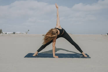 Weibliche Athletin übt Yoga auf einer Übungsmatte am Strand - OIPF00650