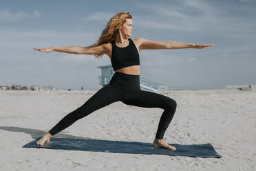 Woman exercising on mat at beach during sunny day - OIPF00653