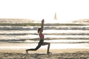 Woman practicing yoga on sea shore during sunny day - OIPF00661