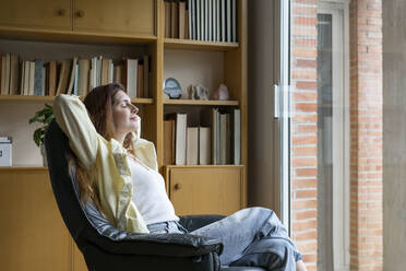 Entspannte Frau sitzt auf einem Stuhl zu Hause - AFVF08733