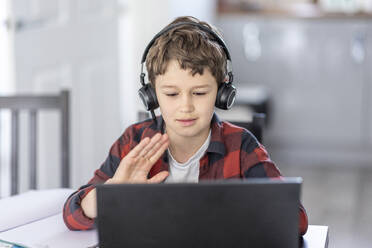 Cute boy waving during video call through laptop at home - WPEF04370