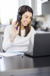 Smiling female professional waving during video conference through laptop at home - WPEF04388