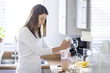 Frau bei der Zubereitung eines Milchshakes in der heimischen Küche zu Hause - WPEF04400