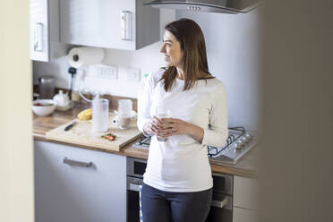 Lächelnde Frau träumt, während sie einen Milchshake in der Küche zu Hause trinkt - WPEF04407