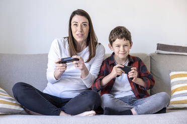 Excited woman and son playing video game while sitting on sofa in living room - WPEF04410