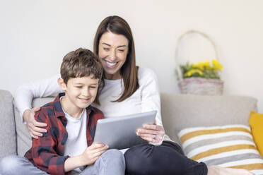 Lächelnder Junge und Mutter verwenden digitales Tablet auf dem Sofa zu Hause - WPEF04415