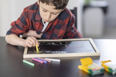 Junge zeichnet mit bunten Kreiden auf Schiefer zu Hause - WPEF04424