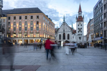 Incidental people walking on footpath during dusk at Marienplatz with Old Town Hall of Munich, Bavaria, Germany - TAMF02946