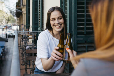 Junge Frauen stoßen mit Bierflaschen an, während sie auf dem Balkon sitzen - XLGF01749