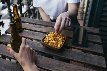 Zwei Frauen genießen ein Bier und essen einen Snack auf dem Balkon - XLGF01751