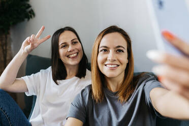 Smiling girlfriends taking selfie at home - XLGF01760