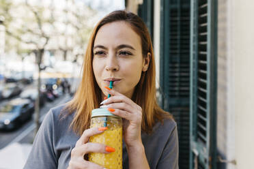 Beautiful woman drinking fruit juice on balcony - XLGF01767