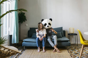 Frau mit Panda-Maske und Friedenszeichen, während sie mit ihrer Freundin zu Hause sitzt - XLGF01773