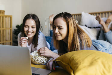 Lächelnde Freunde, die Popcorn genießen, während sie einen Film im Schlafzimmer ansehen - XLGF01778