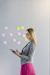 Female entrepreneur looking away holding digital tablet by wall at office - BMOF00574