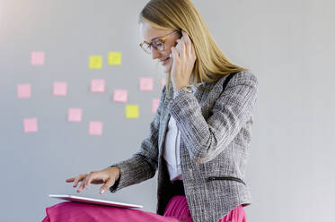 Female entrepreneur talking on smart phone while using digital tablet at office - BMOF00581