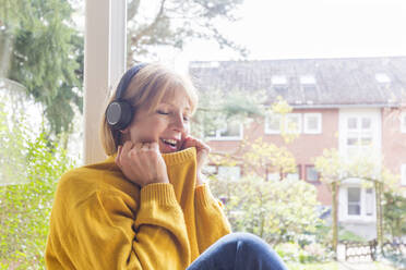 Mature woman with eyes closed listening music through headphones at home - IHF00457