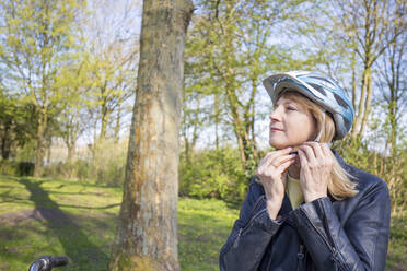 Ältere Frau, die den Helmgurt an einem Baum befestigt - IHF00467