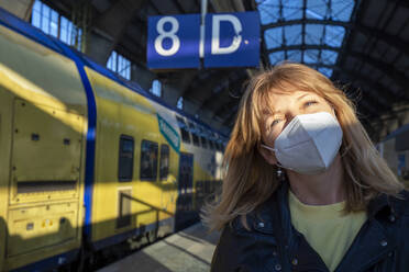 Mature woman wearing protective face mask at railway station during pandemic - IHF00474