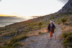 Ältere Frau mit Wanderstöcken auf einem Wanderweg in der Nähe der Adria in Omis, Dalmatien, Kroatien - MAMF01766