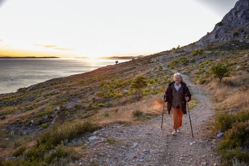 Ältere Frau mit Wanderstöcken auf einem Wanderweg in der Nähe der Adria in Omis, Dalmatien, Kroatien - MAMF01766