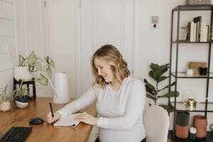 Junge Frau schreibt zu Hause auf dem Tisch in ihr Tagebuch - SMSF00535