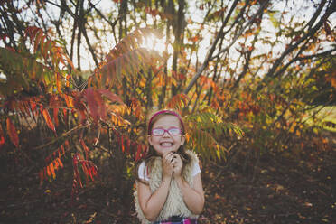 Smiling girl wearing eyeglasses in front of plants during autumn - JBRF00002