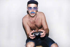Junger schwuler Mann mit Gamecontroller, der auf einen weißen Hintergrund starrt - ASGF00281