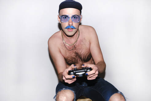 Young gay man with game controller staring against white background - ASGF00281