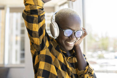 Smiling woman wearing headphones dancing at home - JCCMF02288