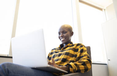Lächelnde Frau mit kariertem Hemd, die zu Hause einen Laptop benutzt - JCCMF02316