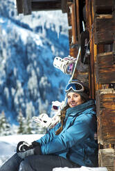 Schöne Frau in warmer Kleidung sitzt bei einer Hütte in Altenmarkt-Zauchensee, Österreich - HHF05603