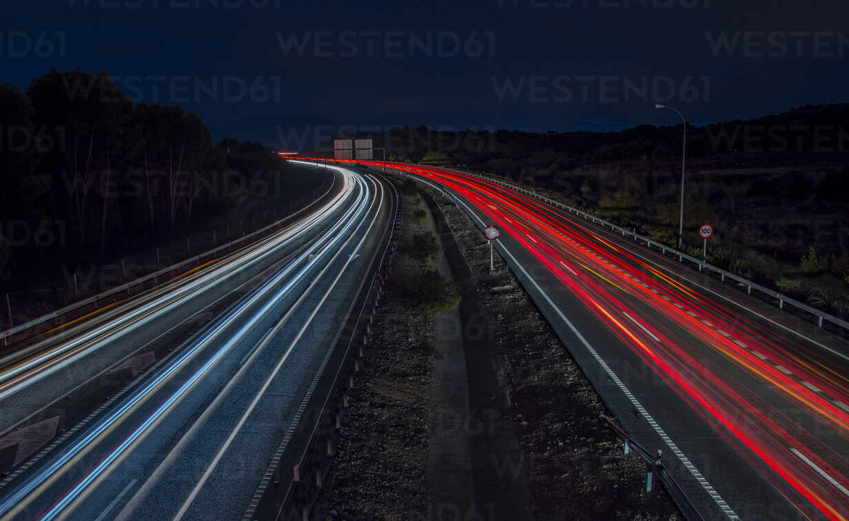 Autoampel auf der Autobahn in der Abenddämmerung. Langzeitbelichtung.  Blaue, weiße und rote Lichter., lizenzfreies Stockfoto