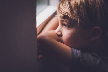 Kleiner Junge mit haselnussbraunen Augen, der aus dem Fenster schaut. - CAVF94053