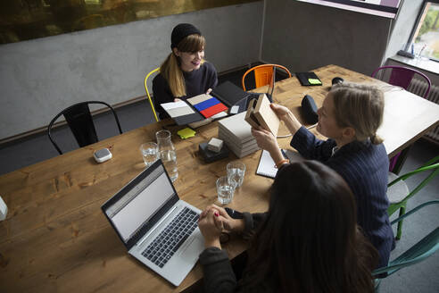 Weibliche Kollegen wählen eine Farbe aus einem Farbmuster aus, während sie am Konferenztisch im Büro diskutieren - MASF23074
