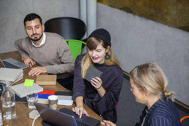 Businesswoman using laptop while discussing with male and female colleagues at creative office - MASF23113